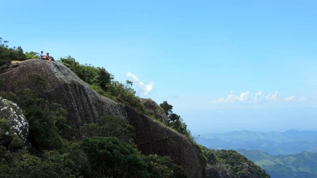 Pessoas sentadas no alto da Pedra Redonda em Monte Verde, Minas Gerais