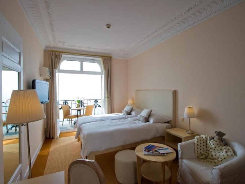 Quarto do Hôtel du Grand Lac Excelsior com cama de casal, varanda e decoração amarelada