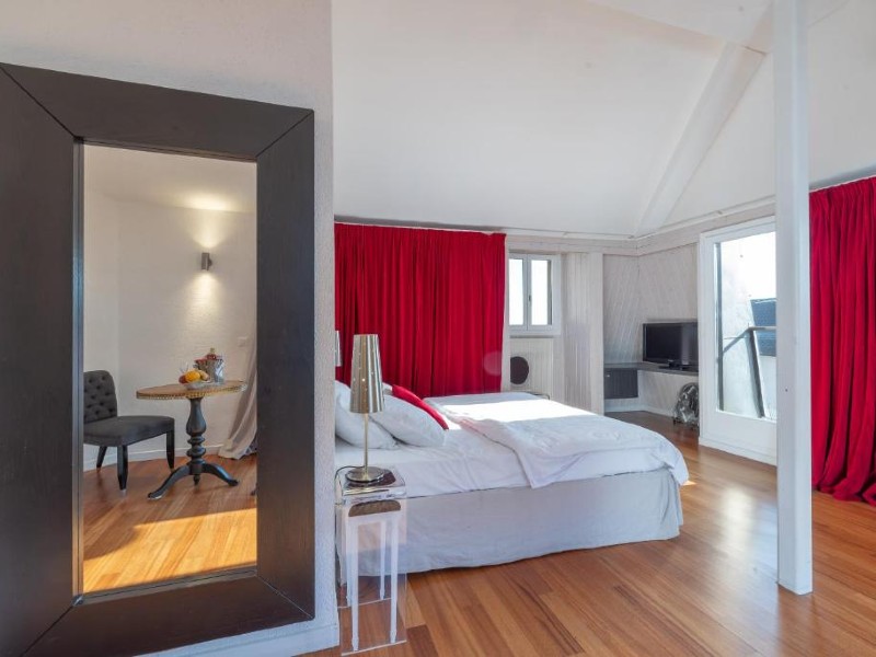 Quarto do Tralala Hotel Montreux com cam ade casal, piso de madeira e cortina vermelha