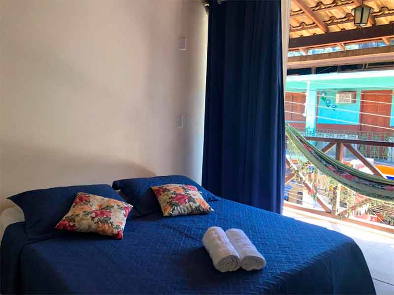Quarto da pousada Porto do Sol com roupa de cama e cortina azul e varanda