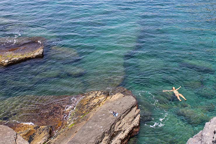 Mulher boia em águas claras próximas da Gruta de Byron, na Itália