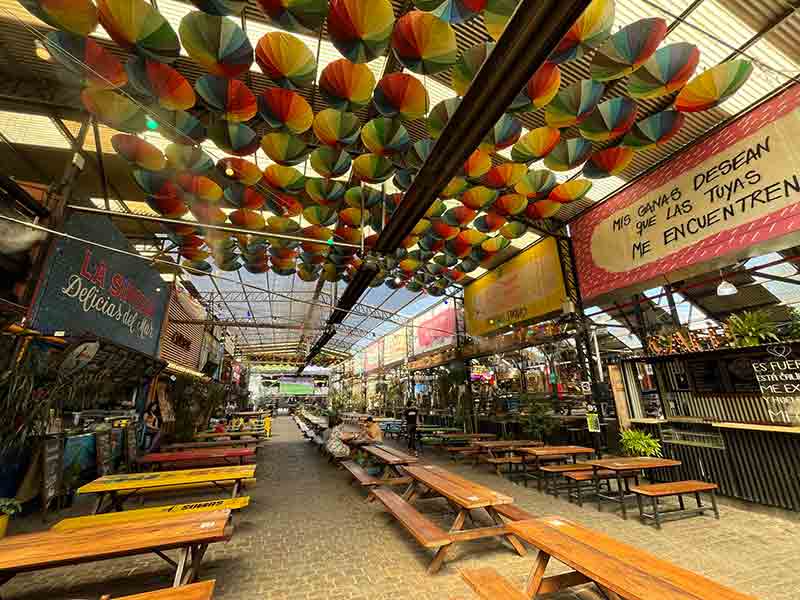 Mesas vazias e teto com guarda-chuvas coloridos no Pátio de los Lecheros
