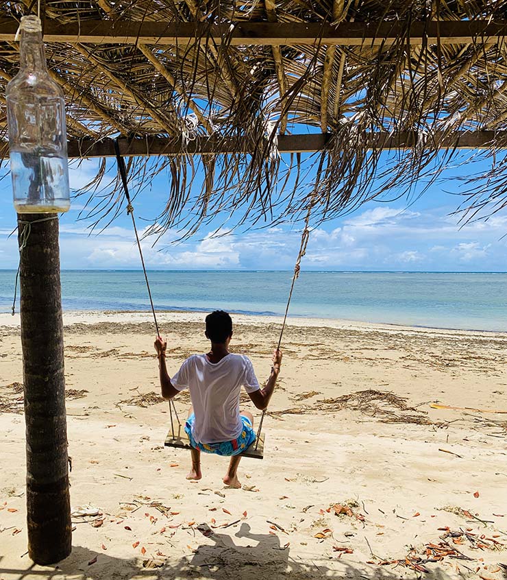 Homem em balanço de frente pro mar da Praia do Bainema em Boipeba