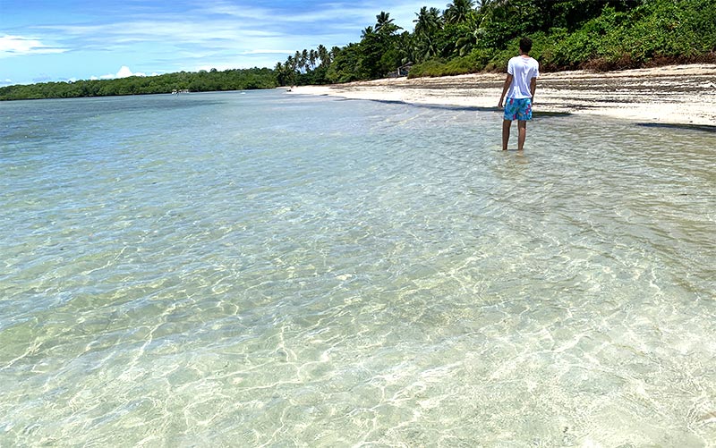 Homem caminhando nas águas cristalinas da Praia do Bainema em Boipeba