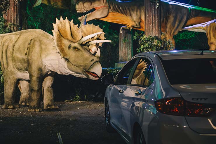 Carro estacionado com dinossauros ao redor