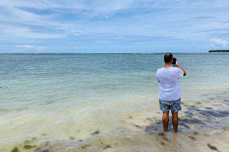 Homem tira foto do mar claro da praia de Tassimirim (Foto: Esse Mundo é Nosso)