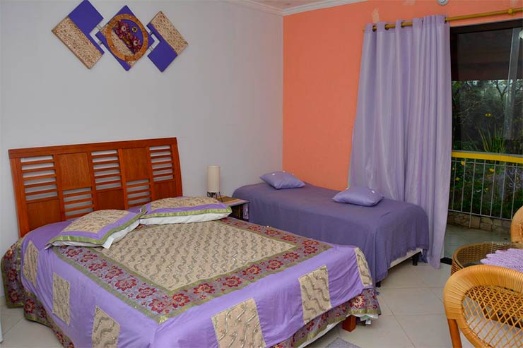 Hotéis e pousadas em São Roque: Quarto com cama de casal e roupa de cama em tons de roxo da pousada Canto das Corujas (Foto: Divulgação)