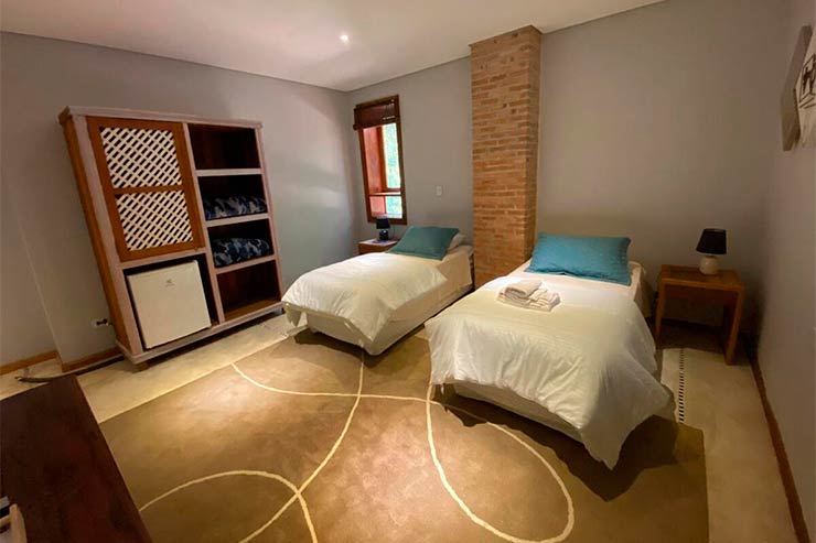 Quarto do Espaço Tajj com duas camas, guarda-roupa e abajur (Foto: Divulgação)