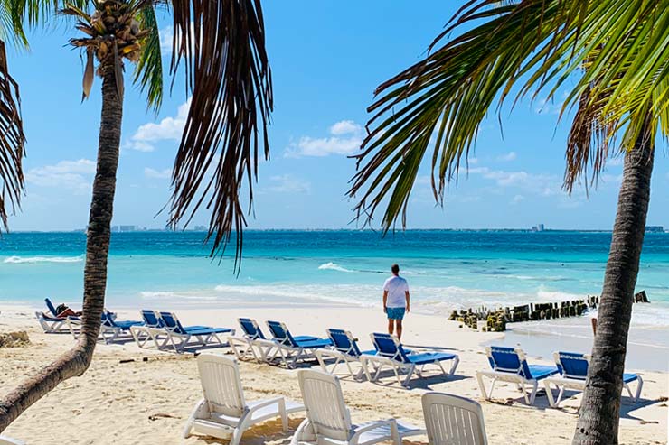 Rafa olhando para o mar entre coqueiros e espreguiçadeiras na Playa Norte, em Isla Mujeres 