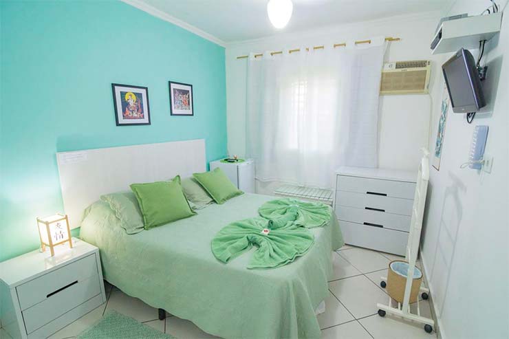 Quarto da Irashai com cama em tons verdes, TV e janela (Foto: Divulgação)