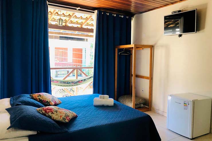 Cama de casal com tons azuis, TV e frigobar da Porto do Sol (Foto: Divulgação)