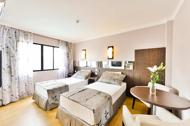 Quarto com duas camas de solteiro e mesa de trabalho com flor no Nadai Confort Hotel e Spa (Foto: Divulgação)