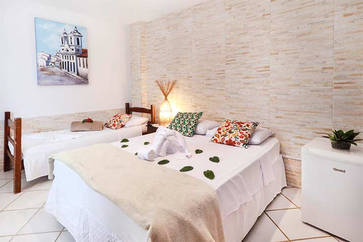 Quarto da Pousada do Mel com cama de solteiro e outra de casal e decoração em tons claros (Foto: Divulgação)