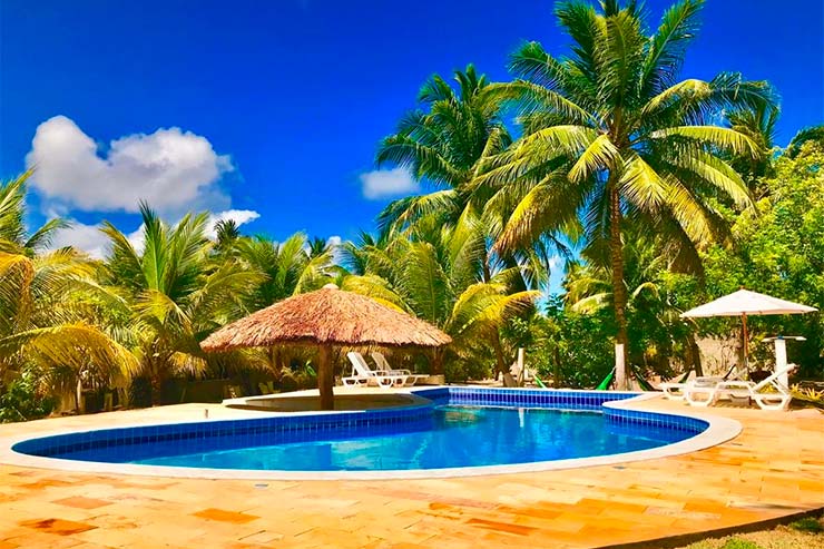 Pousada em São Miguel dos Milagres: Piscina com espreguiçadeiras, árvores e céu azul da Recanto Caiçara (Foto: Divulgação)