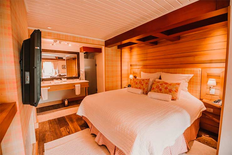 Quarto do Chateau La Villette com cama de casal, banheiro e TV em tons de madeira (Foto: Divulgação)