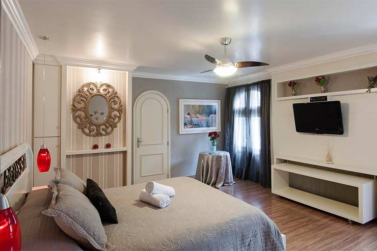 Hotel em Canela: Quarto com cama de casal, TV e decoração em tons brancos e cinza da Doce Canela (Foto: Divulgação)