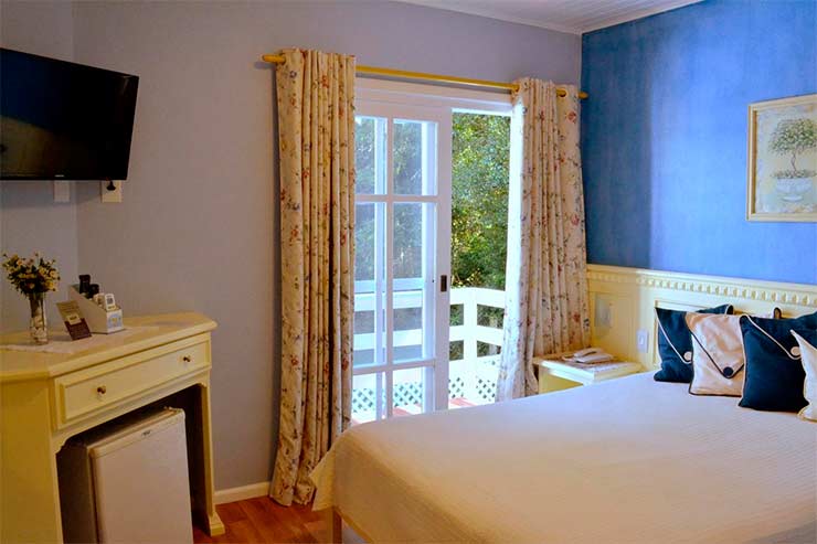 Hotel em Canela: Quarto da Pousada Jardim Azul com parede azul, cama de casal, TV e frigobar (Foto: Divulgação)