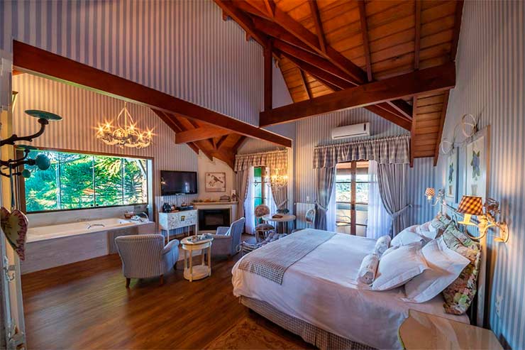Onde ficar em Gramado: Quarto espaçoso da Casa da Montanha com piso de madeira, lareira e cama de casal (Foto: Divulgação)