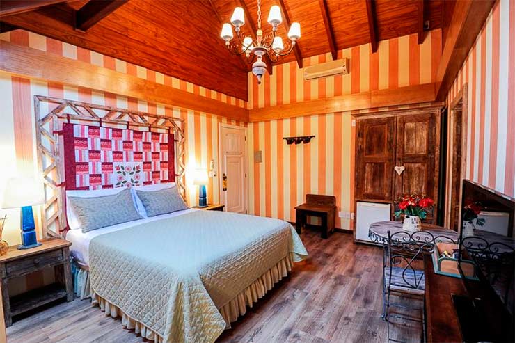 Onde ficar em Gramado: Quarto com cama de casal, TV, frigobar e mesa do Petit Casa da Montanha (Foto: Divulgação)