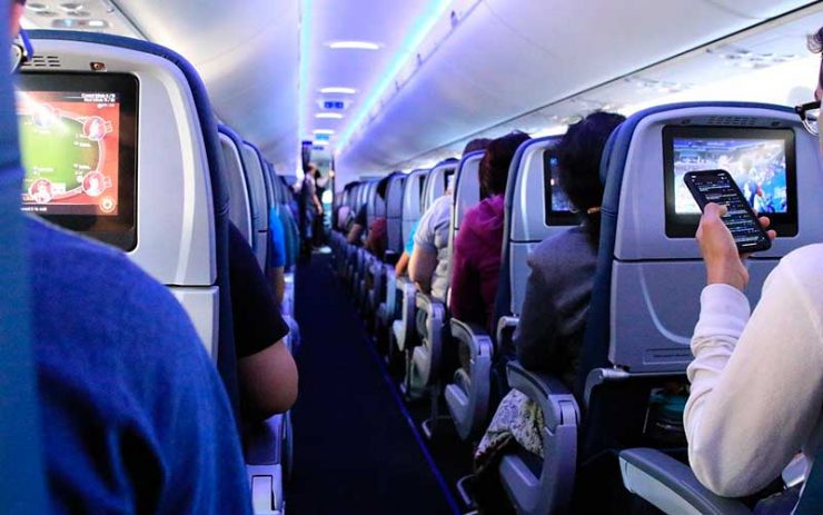 Cabine de voo com passageiros sentados mexendo na tela de entretenimento e no celular