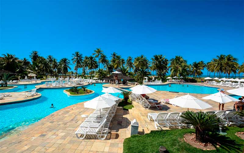 Área da piscina do Sauípe Resorts com espreguiçadeiras, coqueiros e céu azul