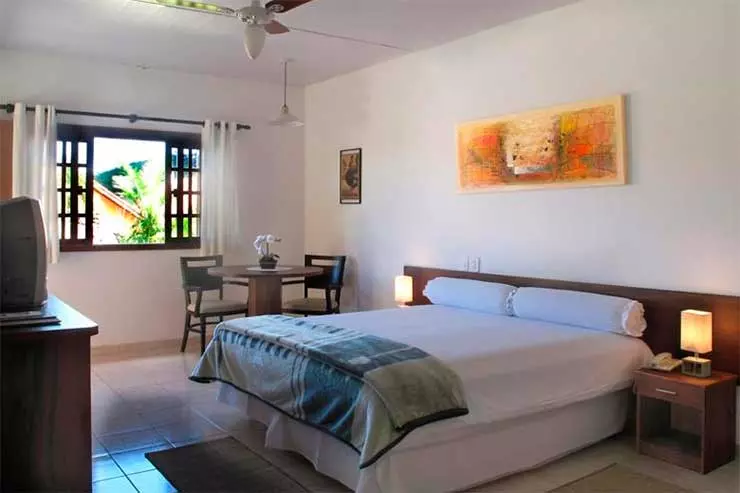 Quarto simples do hotel Monte das Oliveiras com cama de casal, TV de tubo e ventilador de teto