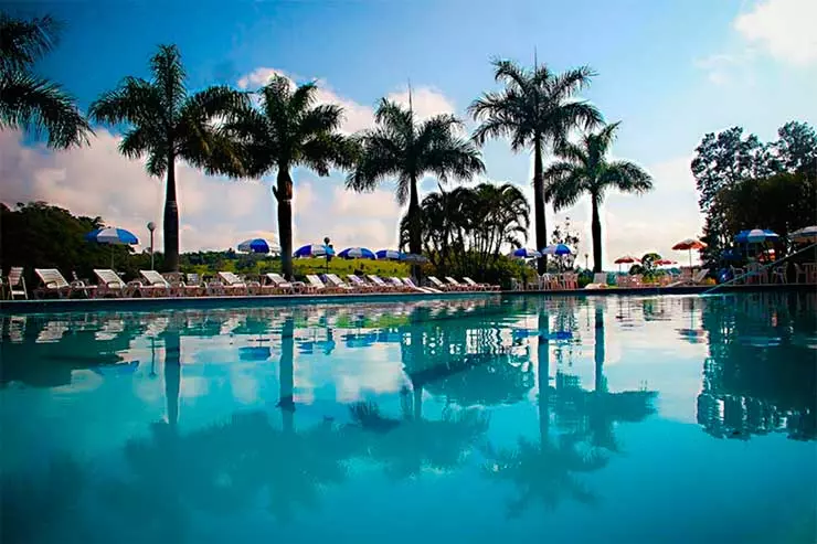 Grande piscina do hotel Península, em Avaré, com árvores e espreguiçadeiras em dia de céu com poucas nuvens