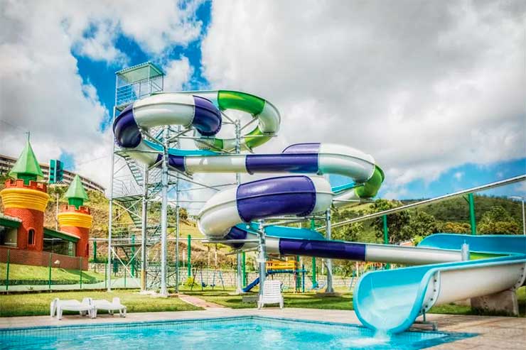 Parque aquático do Village Inn com toboágua e piscina em dia de céu azul com nuvens