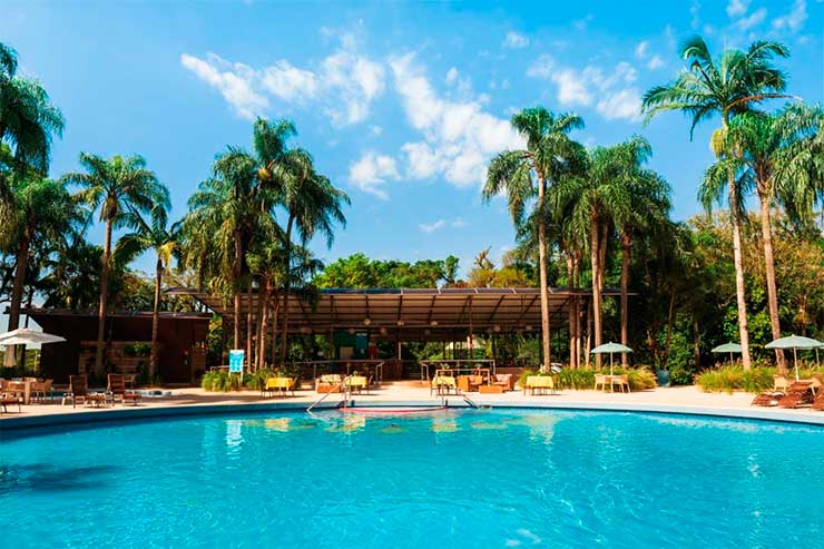 Piscina do Vivaz, em Foz do Iguaçu, com árvores e espreguiçadeiras em dia de céu azul