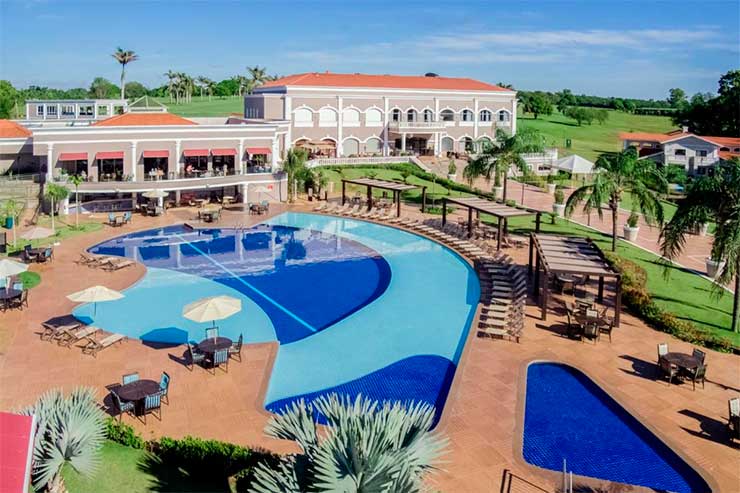 Melhor resort do Brasil: Área da piscina do Wish Foz do Iguaçu com mesas e jardim em dia de céu azul