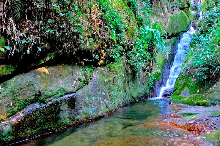 Queda d'água da Cachoeiras das Muralhas em meio à área verde e pedras no Vale do Alcantilado