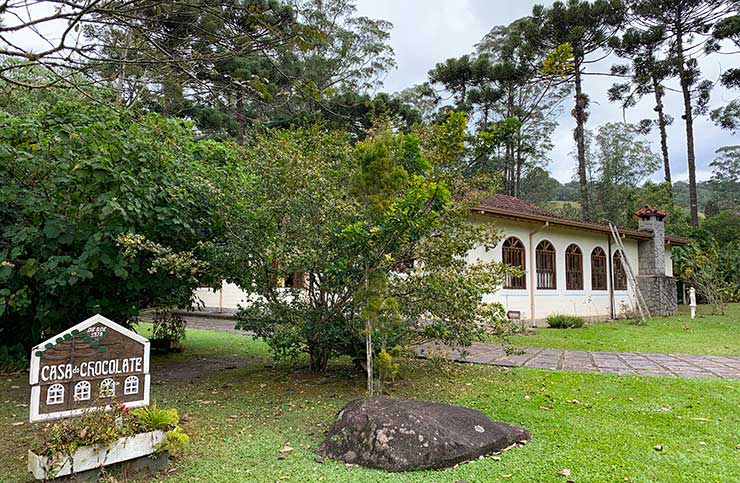 Parte externa da Casa do Chocolate, em Visconde de Mauá, com jardim, árvores e placa com o nome do estabelecimento