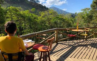 Área externa do Cogumelo Bistrô, em Maromba, com homem sentado à mesa e vista para a natureza