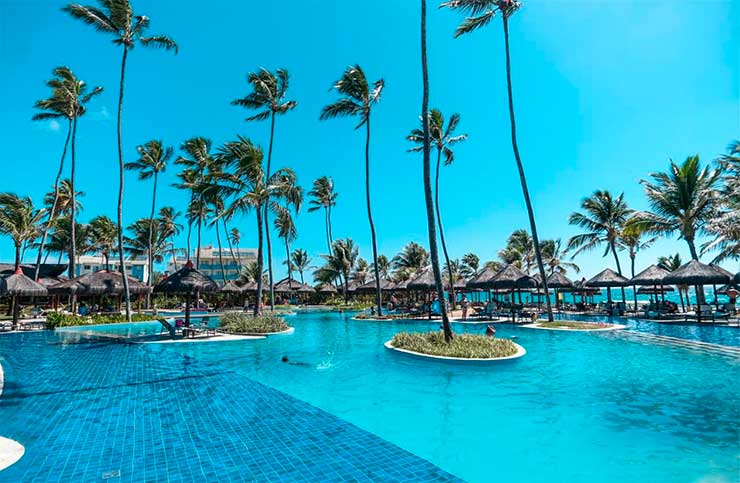 Piscina do Enotel com coqueiros ao redor em dia de céu azul