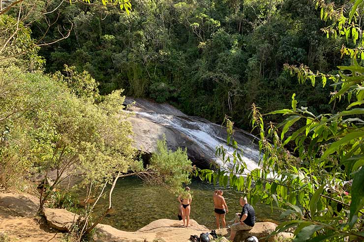 Cachoeiras em Visconde de Mauá: Pessoas sentadas e em pé nas pedras em meio a árvores e em frente à Cachoeira do Escorrega