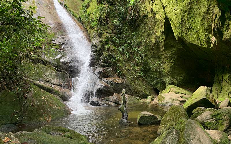 Gruta do Granito, no Vale do Alcantilado, com queda d'água e gruta em meio a pedras e verde 