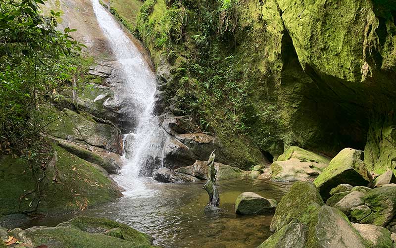 Cachoeira da Gruta do Granito com queda d'água entre as pedras e gruta à direita
