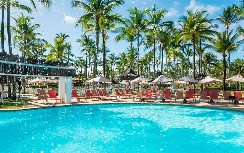 Piscina do Transamérica Comandatuba com coqueiros e espreguiçadeiras em dia de céu azul