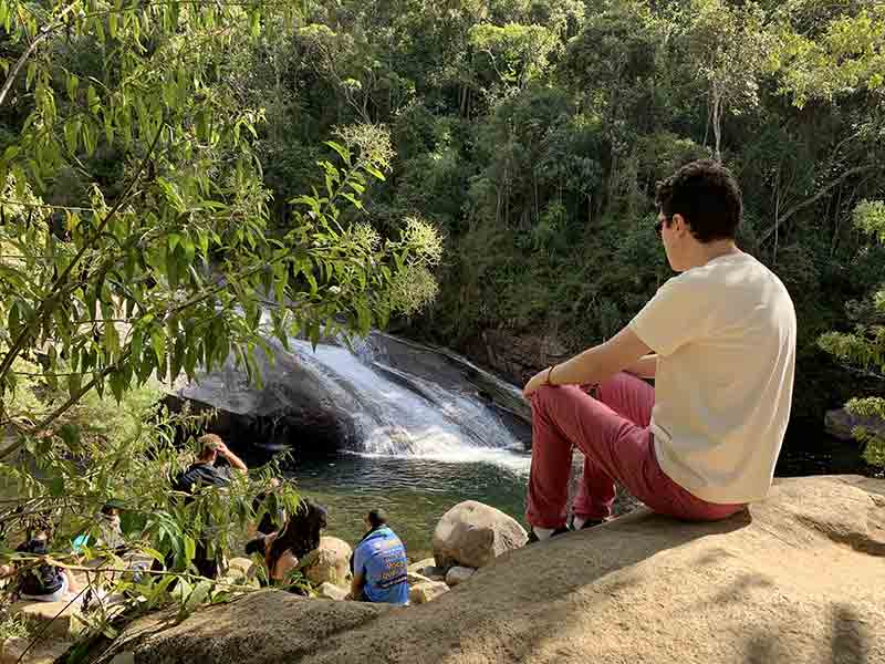 Homem sentado na pedra da Cachoeira do Escorrega em Visconde de Mauá