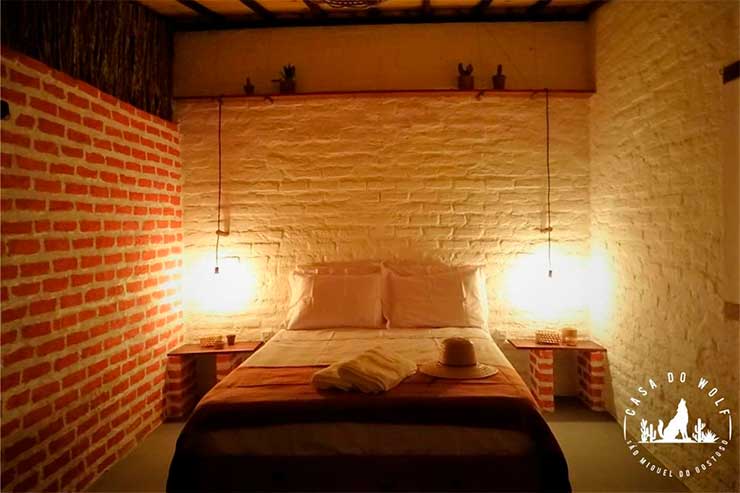 Quarto da Casa do Wolf com cama de casal, luminárias e tijolos