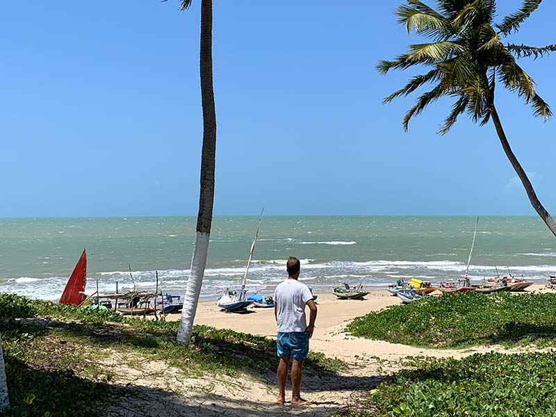 Praia de Zumbi com homem entre coqueiros de frente pro mar