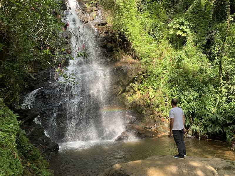 Rafael em pé em frente à Cachoeira do Véu de Noiva em Maromba