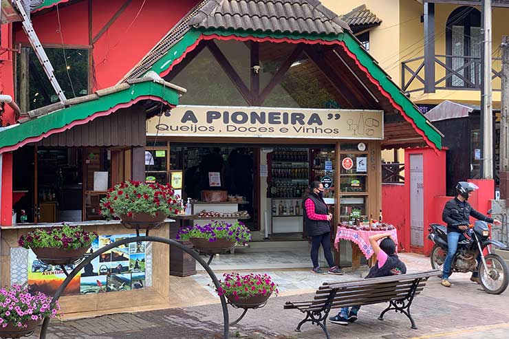 Entrada da A Pioneira, uma das lojas em Monte Verde, com mulher na porta ao lado de uma moto