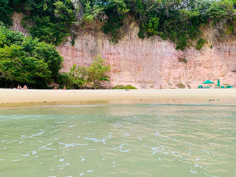 Mar esverdeado com falésias na frente e areia na Baía dos Golfinhos