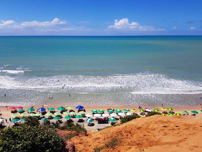 Guarda-sóis coloridos vistos de cima em frente ao mar na Praia do Amor em Pipa