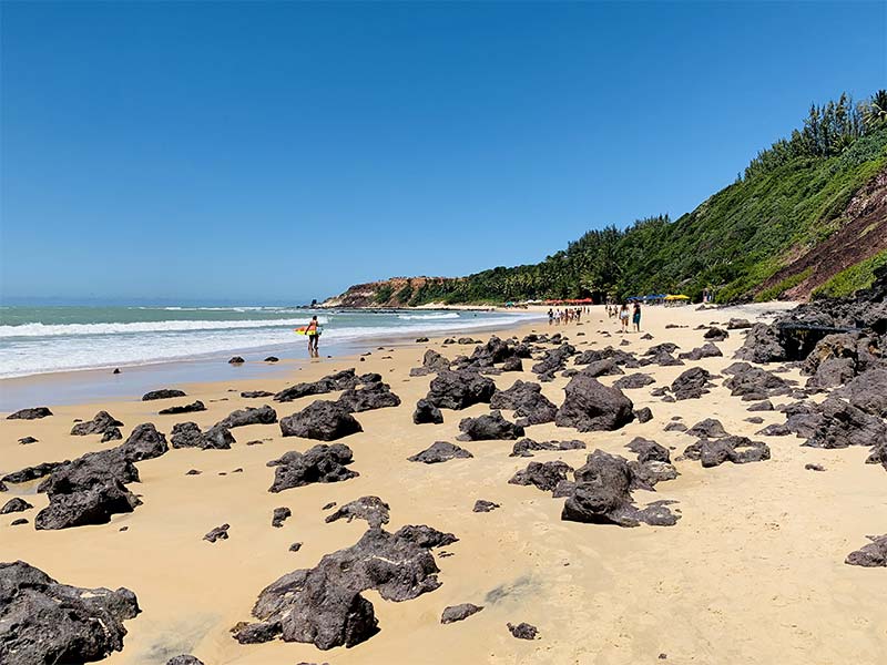 Surfista em meio a pedras na areia em frente ao mar