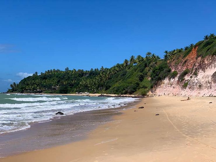 Pessoa toma sol em frente À mar com ondas na Praia do Giz, em Tibau do Sul