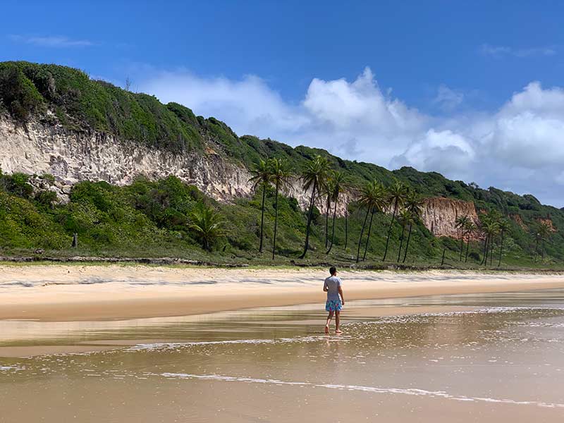 Homem caminha no mar na Praia do Madeiro