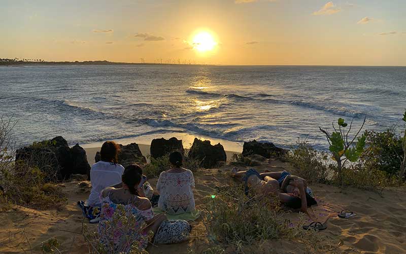 Pessoas deitadas na areia assistem ao pôr do sol na Praia de Tourinhos