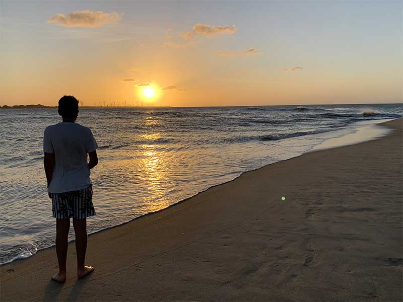 Homem em pé em frente ao mar assiste ao pôr do sol na Praia de Tourinhos
